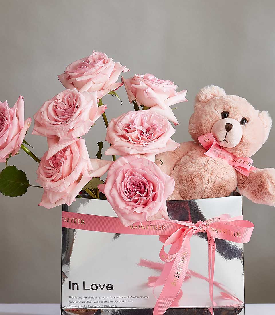 Pink roses and soft teddy bear in silver gift box with pink ribbon, perfect birthday or romantic gift