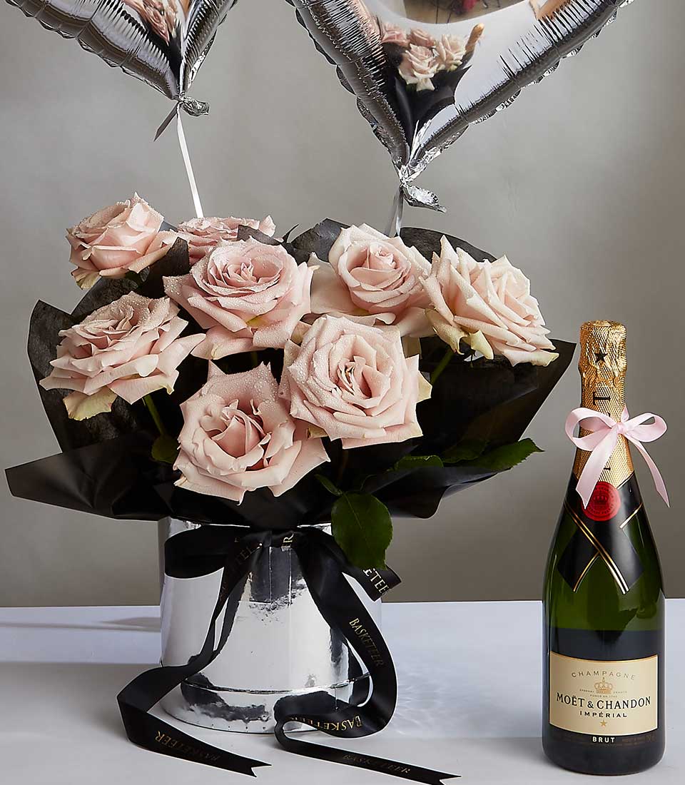 Pale pink rose bouquet with champagne bottle, black ribbon, and gold foil top in silver vase