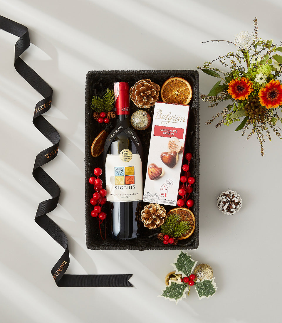Festive red wine gift basket with Belgian chocolates, holiday florals, and seasonal decorations