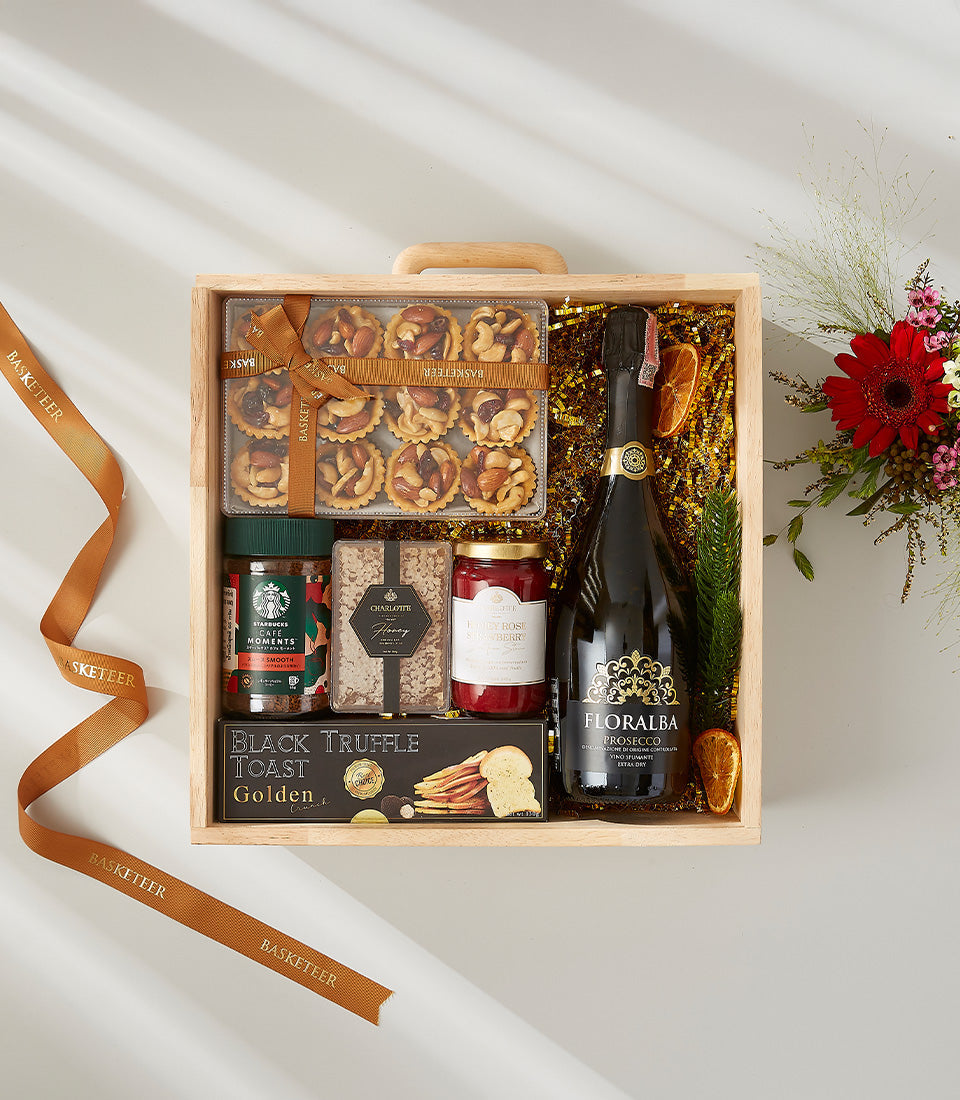 Luxury wooden gift hamper with Prosecco, gourmet tarts, truffle toast, jam, honey biscuits, and coffee on gold shredded paper