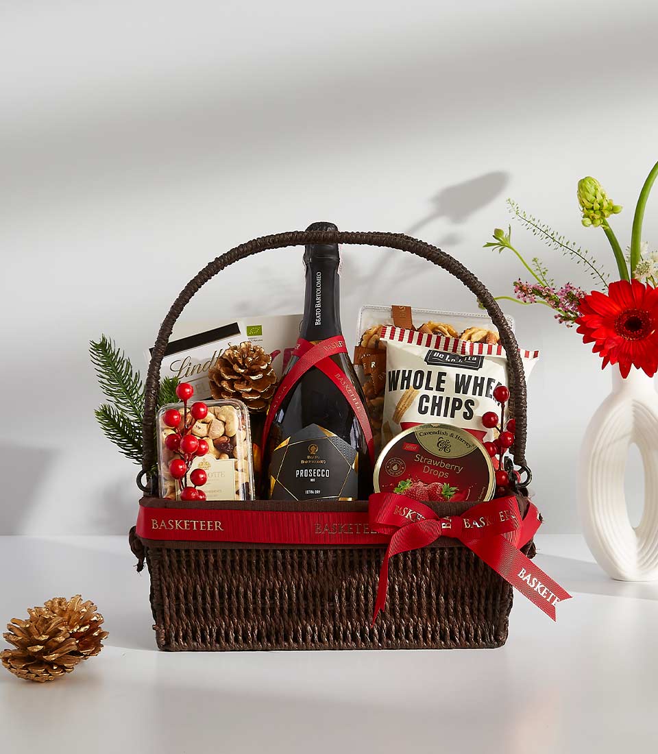 Festive Prosecco gift basket with red gerberas, nuts, and gourmet treats in woven brown basket