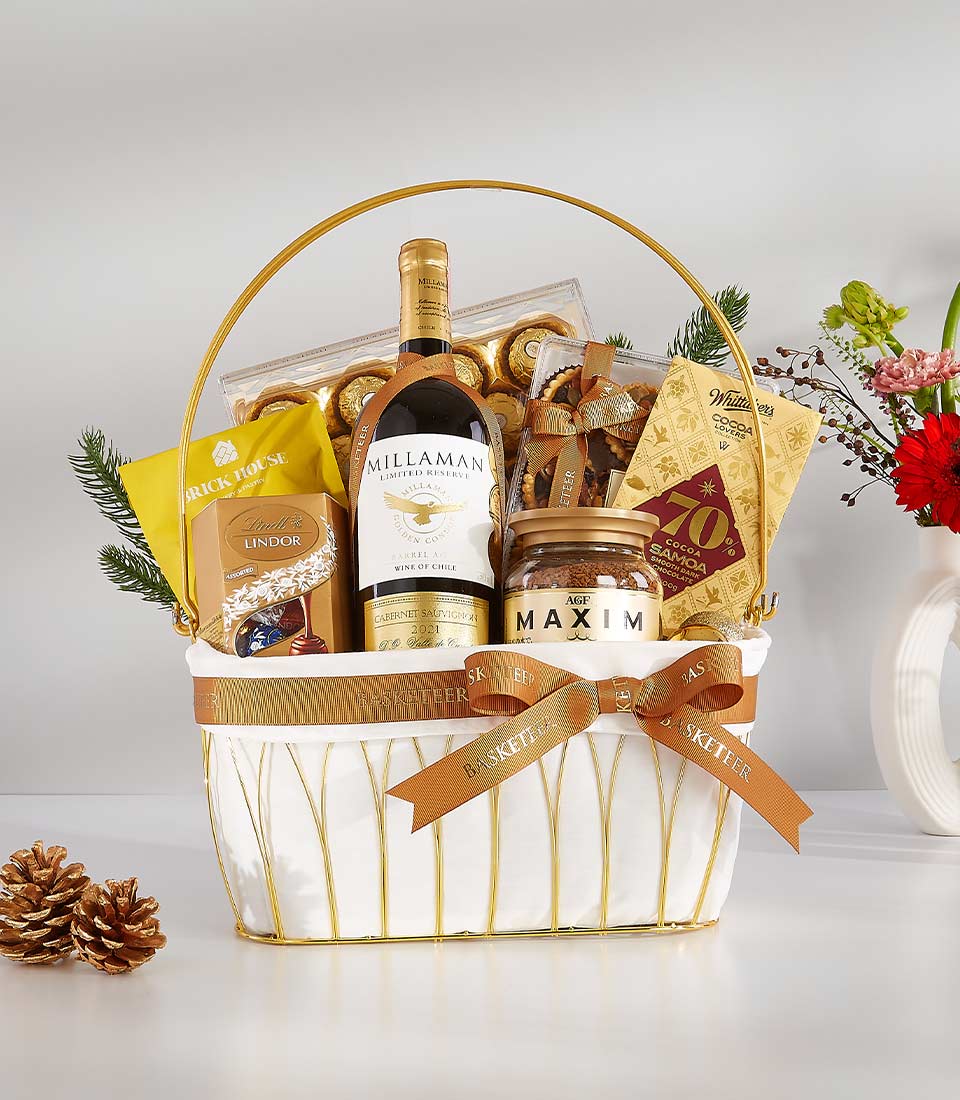 Elegant golden wine gift basket with red wine, gourmet chocolates, coffee, and fresh flowers for celebration gifting