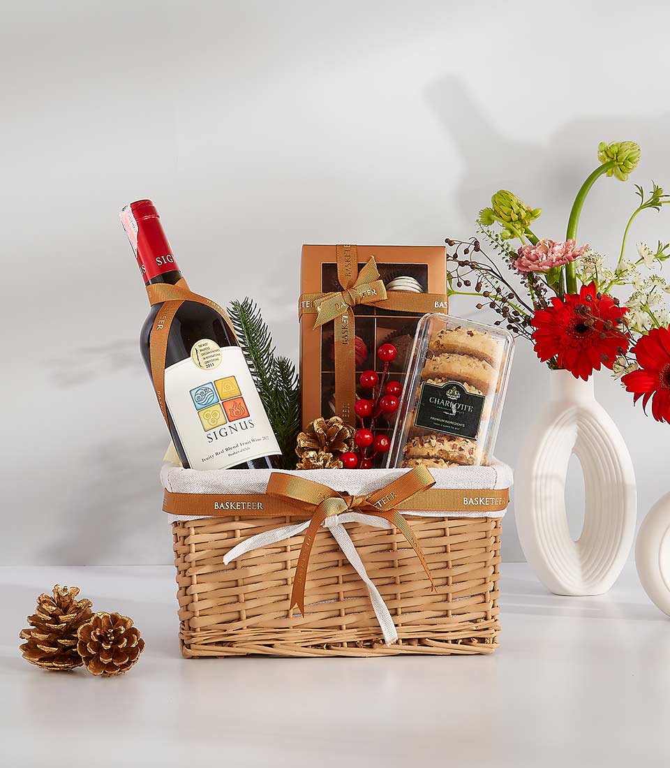 Premium gift basket with red wine, chocolate, and cookies in wicker with gold ribbon and fresh flowers