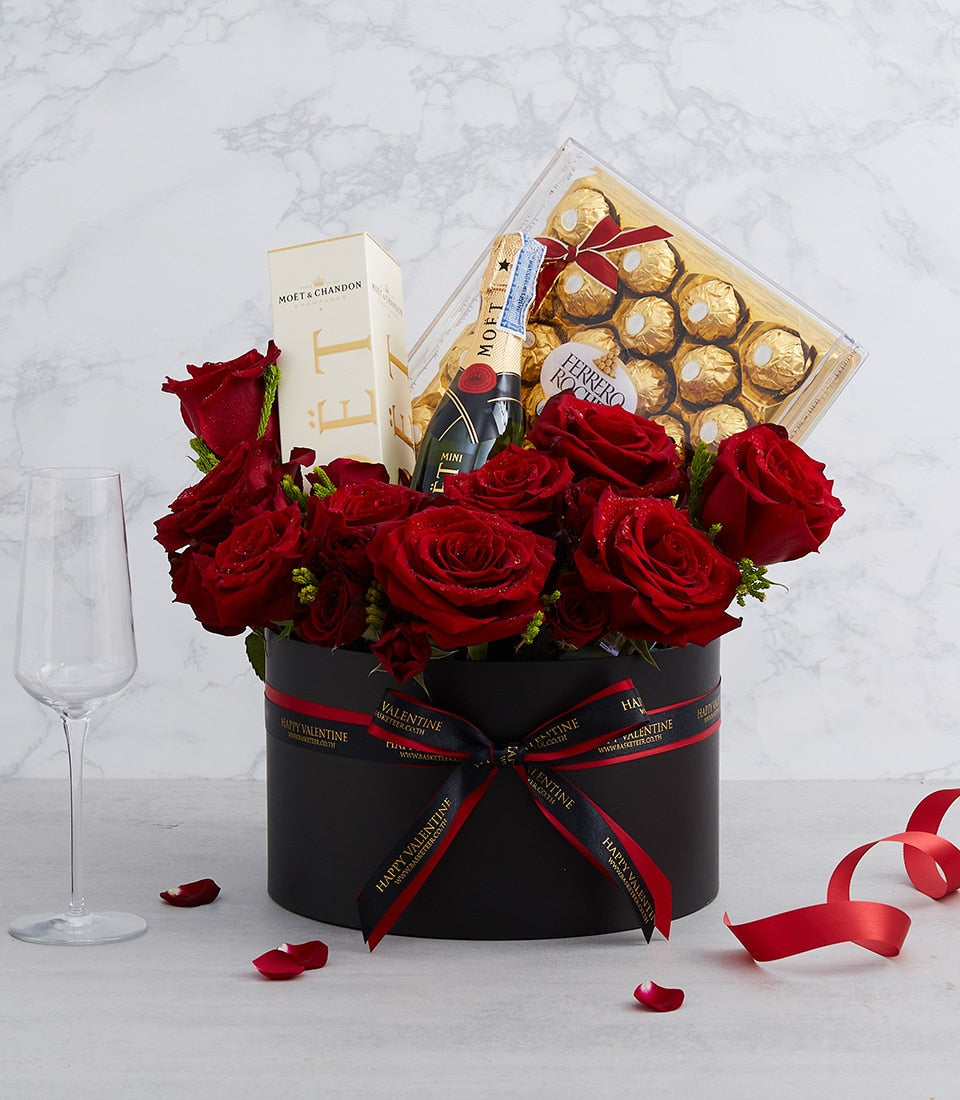 Luxury red roses, champagne, and gold-wrapped chocolates in black cylindrical Valentine gift box