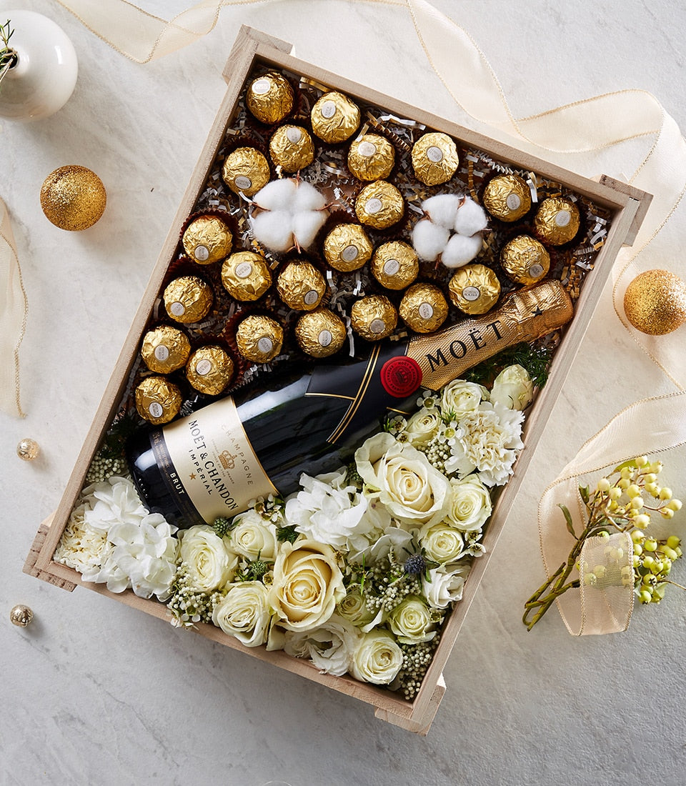 Champagne bottle with gold-foiled chocolates and white roses in wooden luxury gift crate