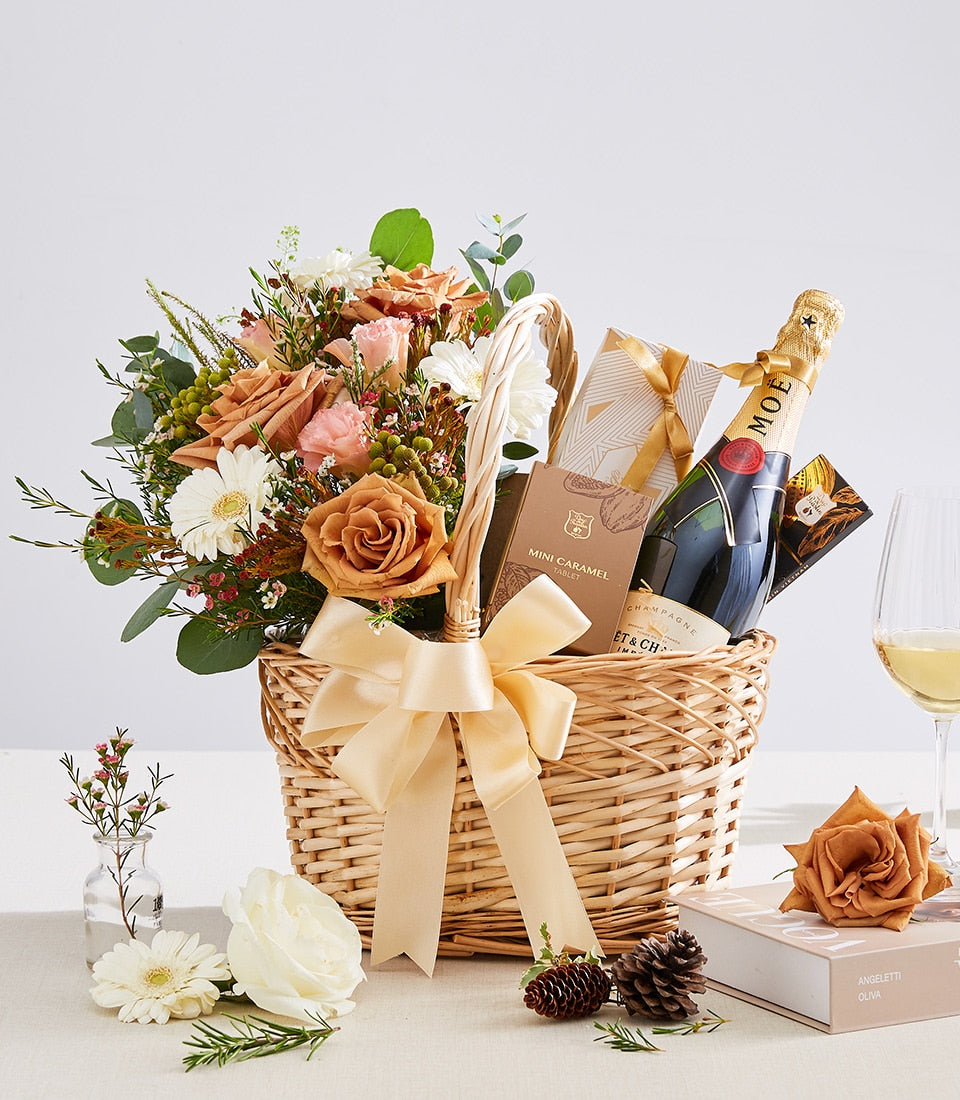 Luxury champagne and floral gift basket with peach roses, daisies, gold-wrapped chocolates, and sparkling wine