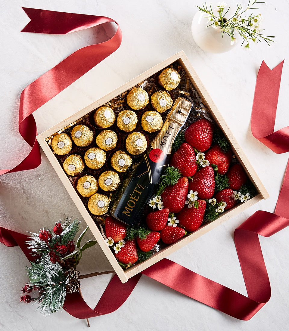 Luxury wooden gift box with champagne, gold-wrapped chocolates, fresh strawberries, and red satin ribbons