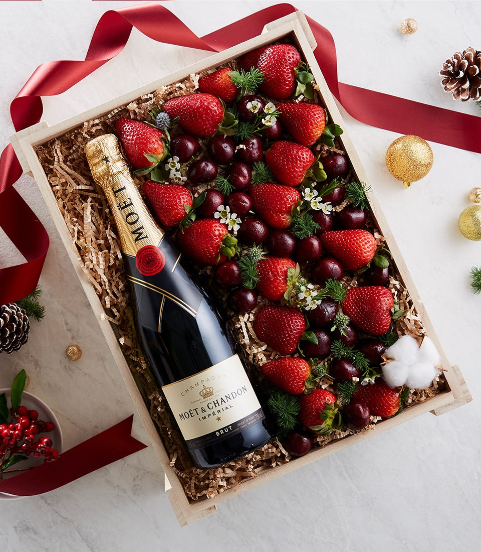 Deluxe champagne bottle with fresh strawberries, cherries, and white flowers in luxury gift box with red satin ribbon