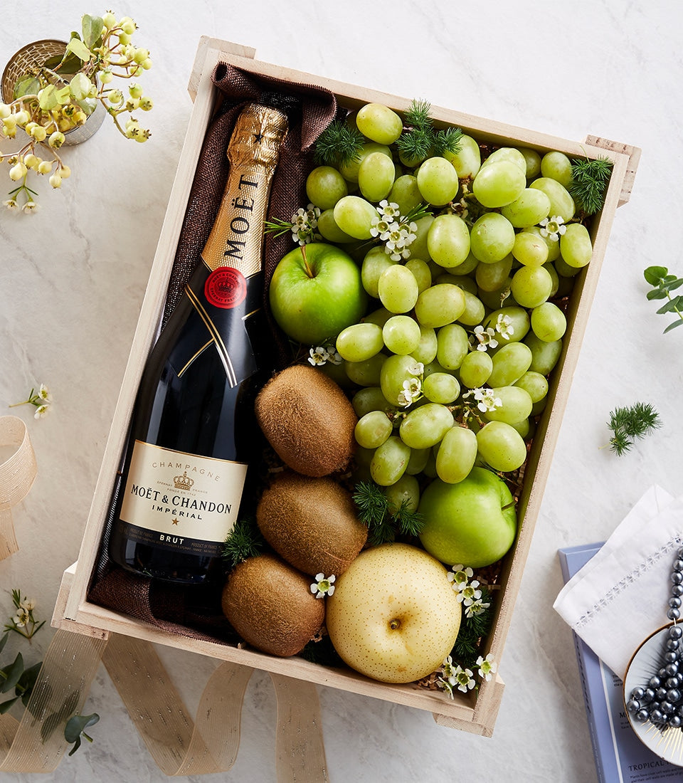 Moët champagne and fresh fruit gift crate with grapes, kiwis, and pears in wooden basket with gold ribbon