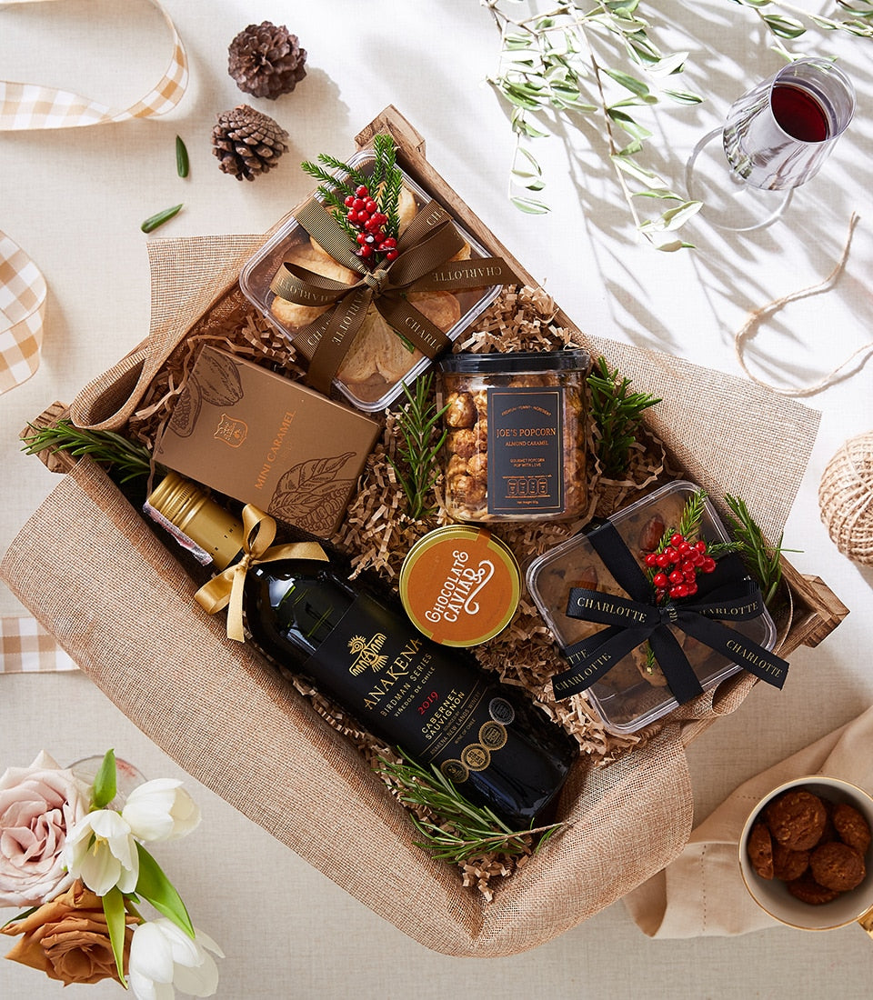 Premium red wine and chocolate gift box with caramel popcorn and baked goods in rustic wooden crate