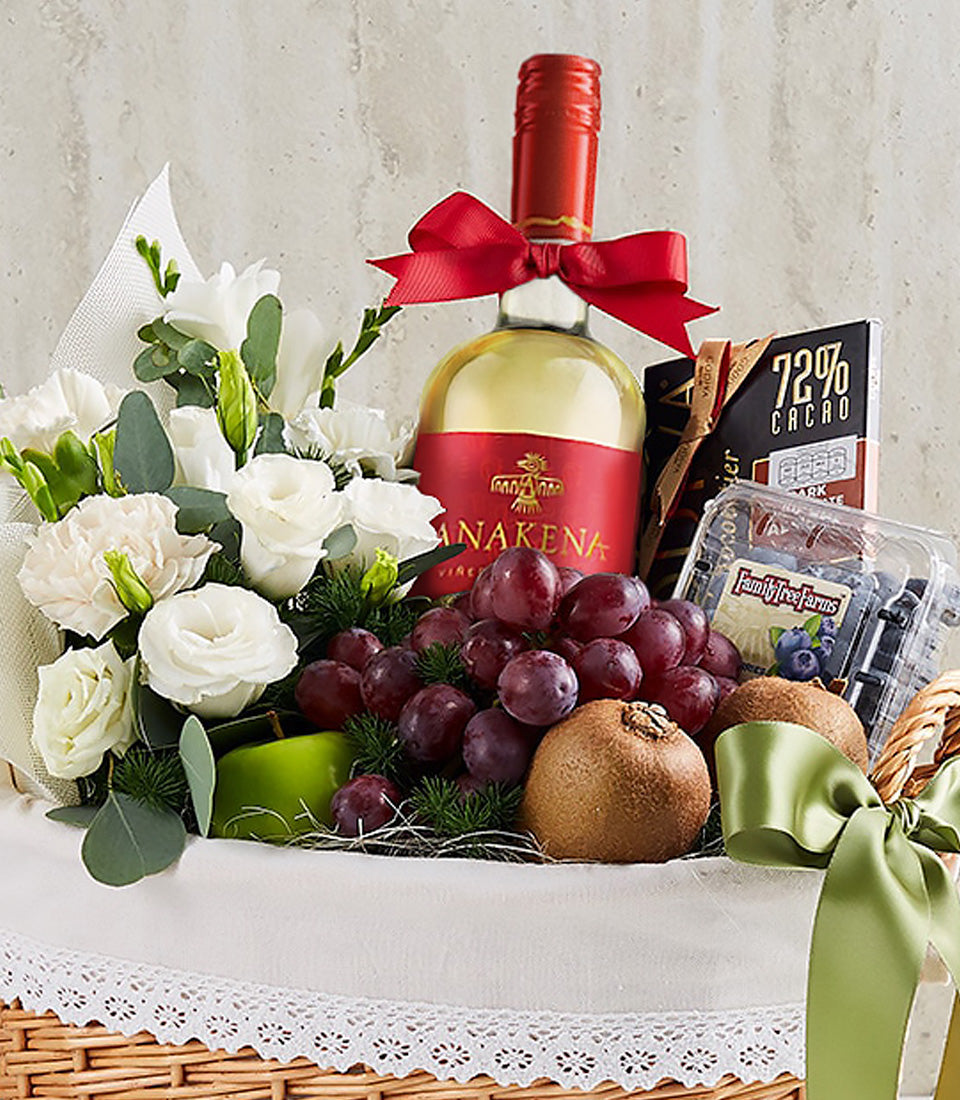 Luxury wine gift basket with white wine, fresh white flowers, red grapes, kiwi, apple, chocolate, and blueberries in wicker