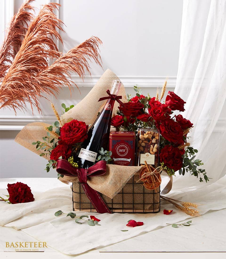 Luxury red wine gift hamper with premium tea, nuts, fresh roses and eucalyptus in wire basket with red satin bow