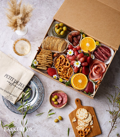 Artisan charcuterie and cheese gift box with olives, cured meats, crackers, fresh fruit, and edible flowers
