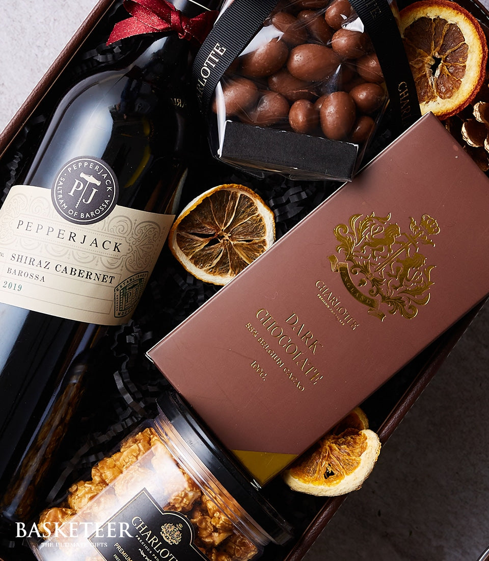 Pepperjack Shiraz with dark chocolate and gourmet snacks in luxury gift hamper, cream ribbon and black shredded paper