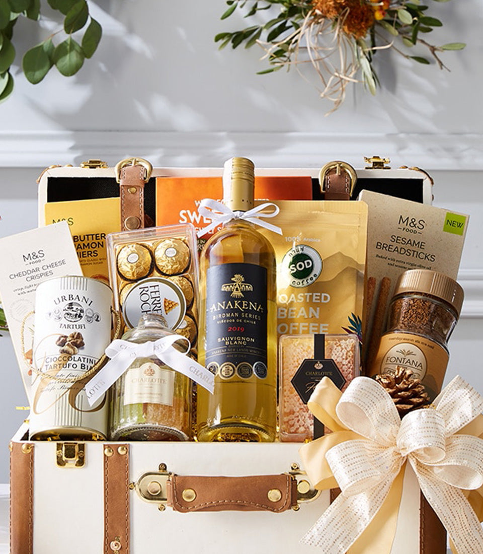 Luxury wine and gourmet gift hamper with white wine, chocolates, coffee, and artisan snacks in leather trunk