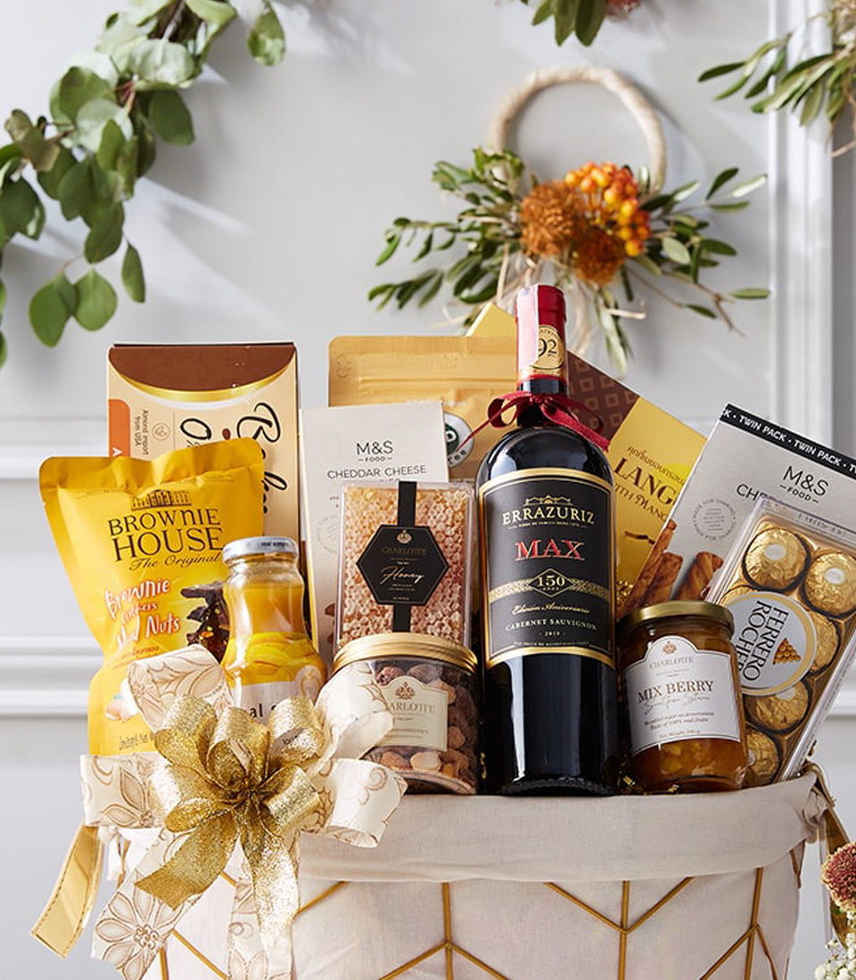 Red wine gourmet gift basket with brownies, honey, nuts, jam, and chocolate in white woven basket with gold bow