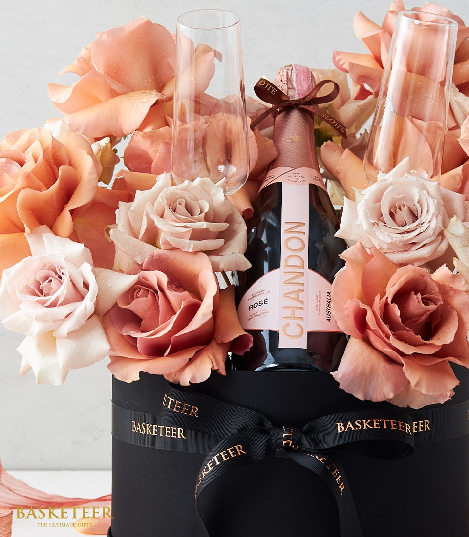Rosé sparkling wine with champagne flutes and fresh peach roses in luxury black gift box