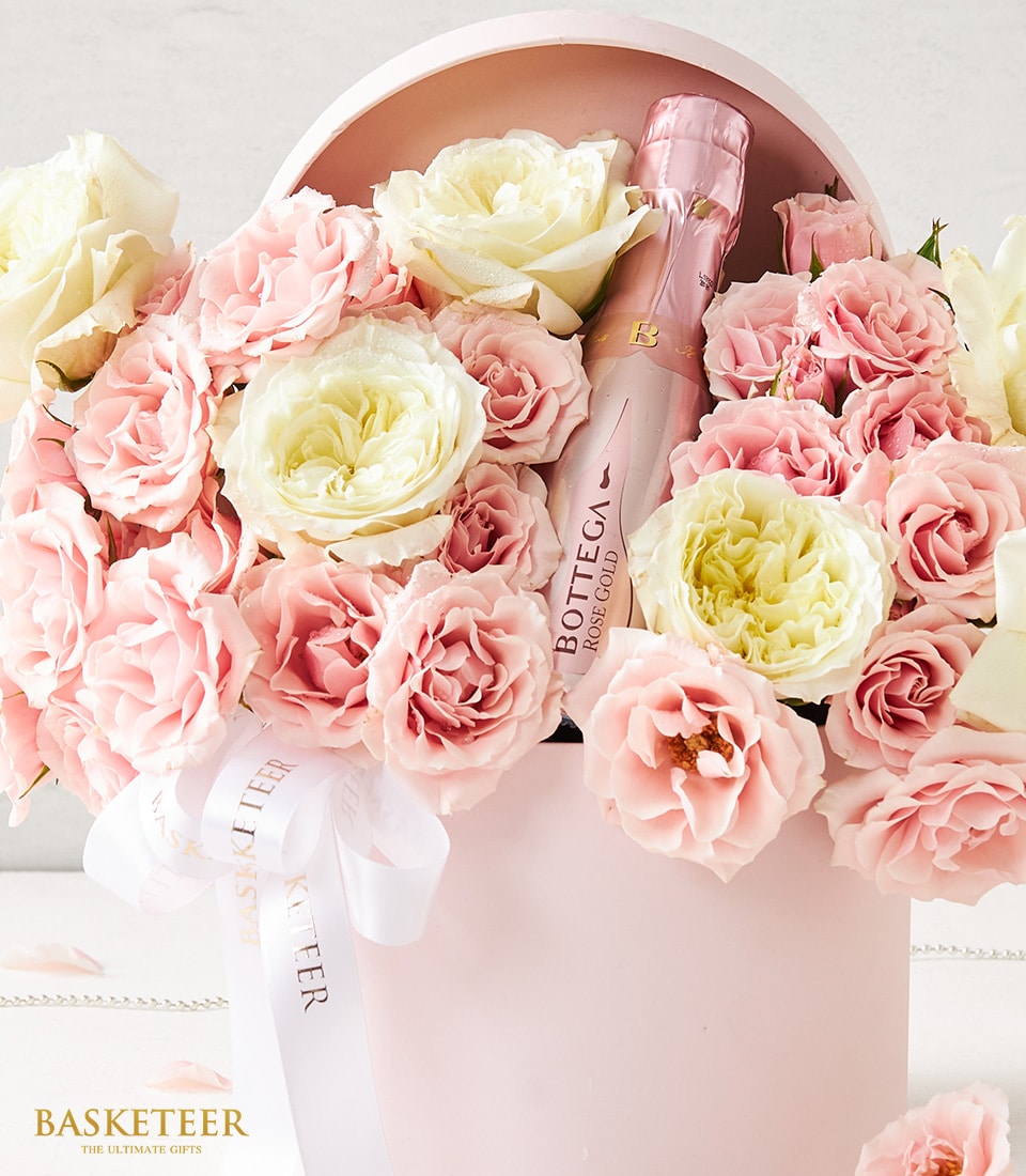 Luxury sparkling rosé wine with fresh blush roses and teddy bear in pink hatbox, anniversary gift set