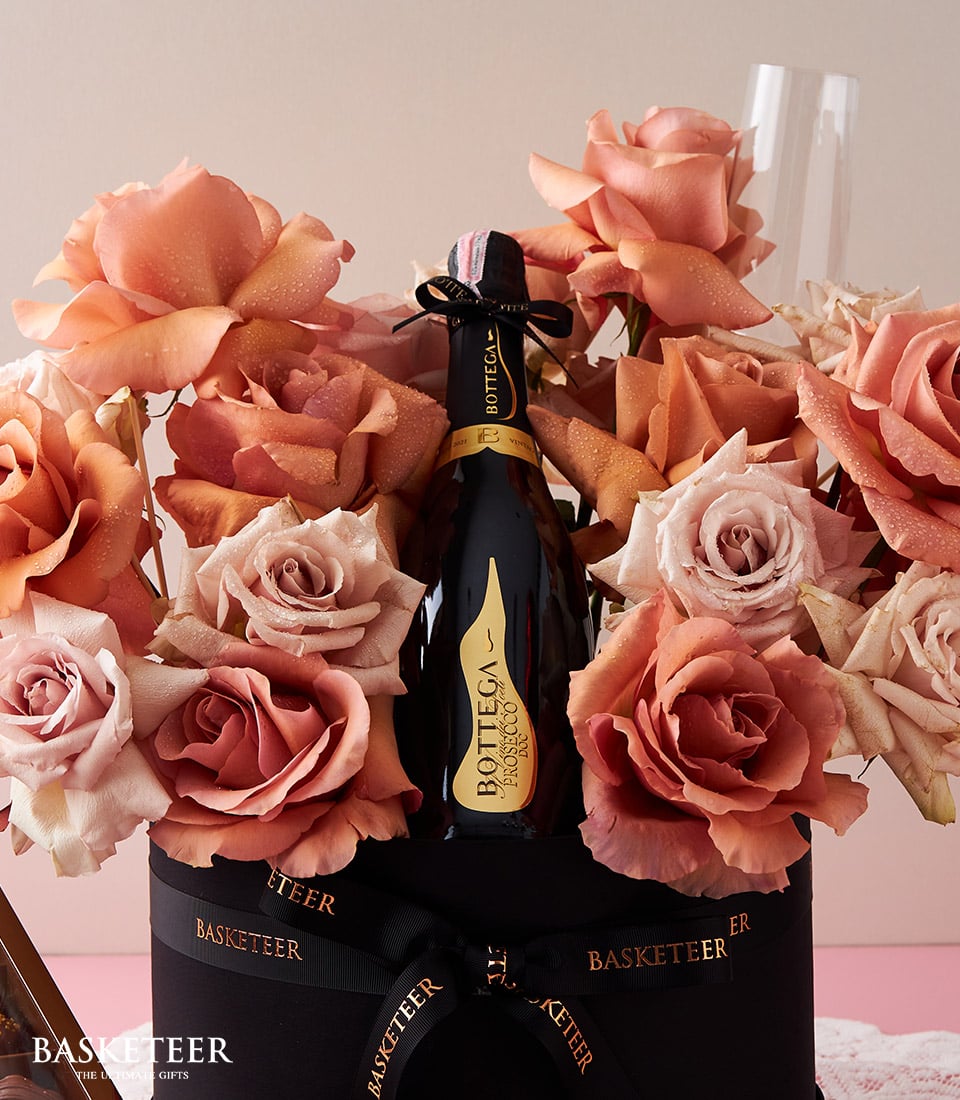 Luxe roses in peach and coral with champagne bottle and artisan chocolates in black gift box for anniversaries