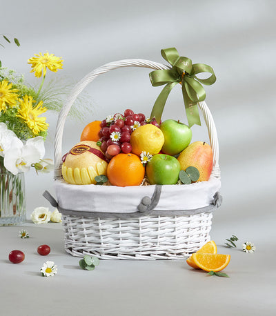White wicker fruit basket with Granny Smith apples, red grapes, citrus, and pears tied with green satin ribbon