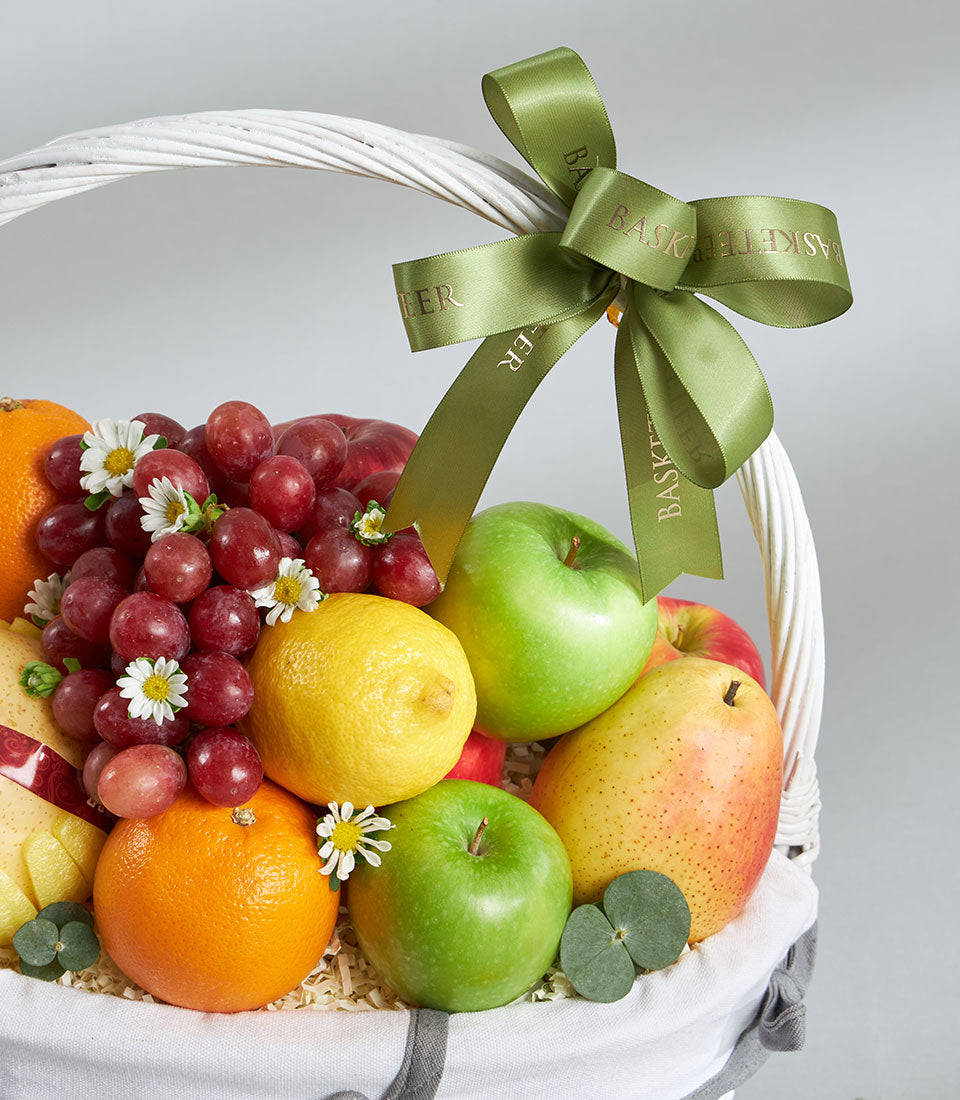 Premium imported fruit basket with Granny Smith apples, red seedless grapes, citrus and fresh flowers in white woven basket