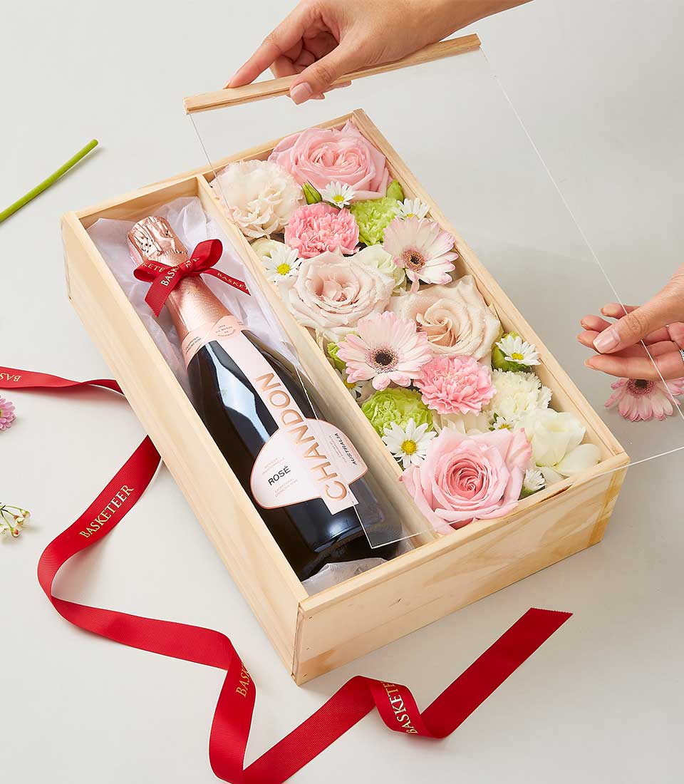 Wooden gift box with rosé champagne and fresh pink roses, carnations, gerbera daisies in clear acrylic case