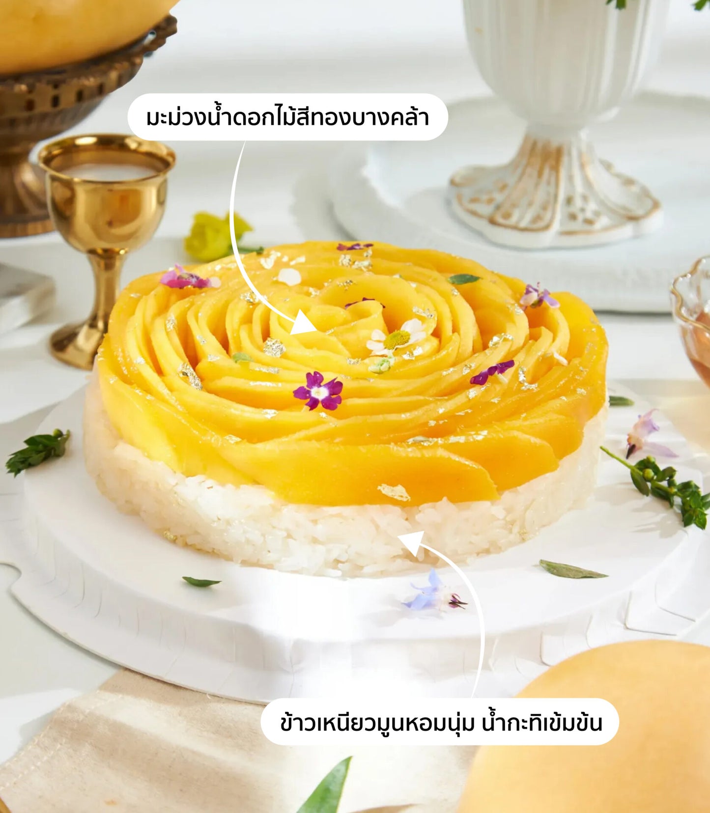 Golden rose mango sticky rice cake with edible silver flakes and fresh flowers on white plate