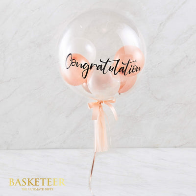 Clear bubble congratulations balloon with nested white, rose gold and pink balloons, tied with peach satin ribbon