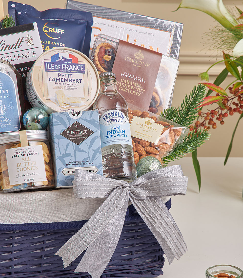 Premium gourmet hamper with sea salt dark chocolate, camembert cheese, and artisan treats in dark blue wicker basket with