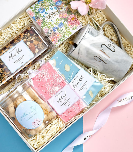 Mother's Day gift box with marble mug, notebook, gourmet cookies, and mixed nuts on pink and blue background