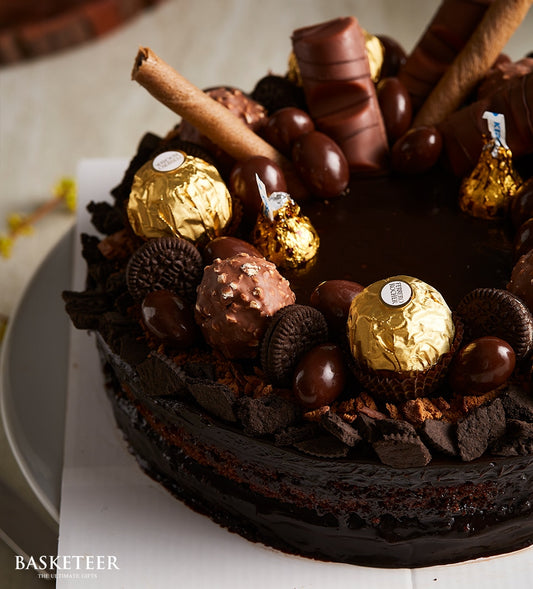 Decadent layered chocolate cake with ganache, topped with gold-foiled chocolates, truffles, and wafer rolls