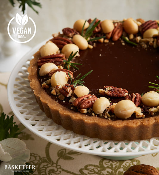 Vegan dark chocolate tart with pecans, macadamia nuts, and fresh rosemary on an ornate white cake stand