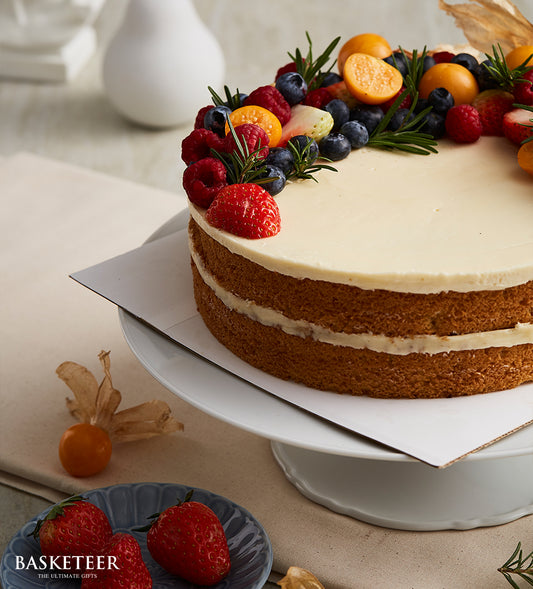 Mixed berry vanilla butter cake with fresh strawberries, blueberries, and rosemary on white frosting