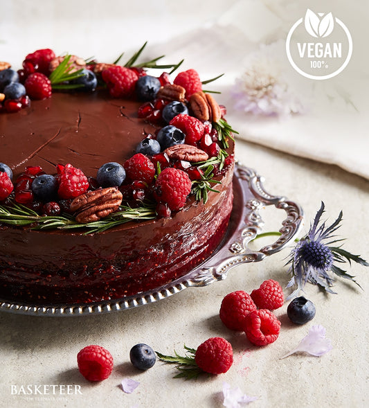 Decadent vegan chocolate cake with fresh berries, nuts, and rosemary on silver platter