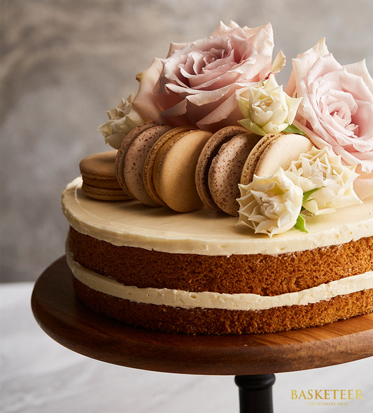 Vanilla butter cake with white frosting, pink roses, and macarons on wooden stand for birthday celebrations