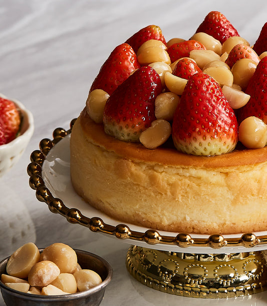 Strawberry macadamia cheesecake with fresh berries and nuts on gold-rimmed cake stand