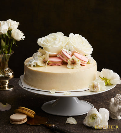 Vanilla mousse cream cake with white roses and pink macarons on ceramic stand, artisan birthday gift