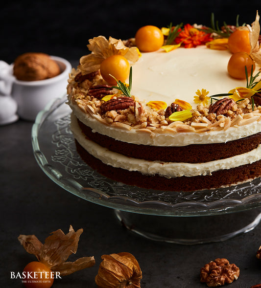 Three-layer naked carrot cake with cream cheese frosting, pecans, almonds, and physalis on glass cake stand