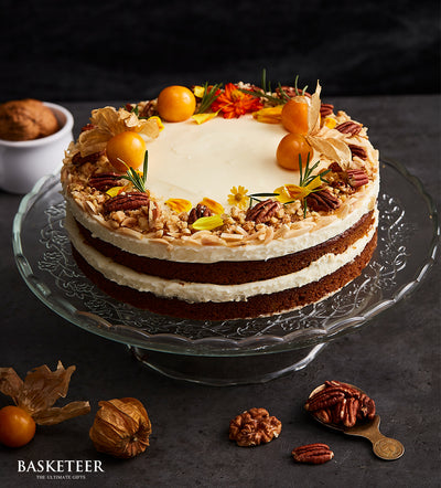 Three-layer carrot cake with cream cheese frosting, pecans, walnuts, and fresh physalis on glass stand