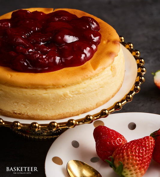 Golden cheesecake with dark red strawberry jam topping on ornate gold stand, fresh strawberries and polka dot plate