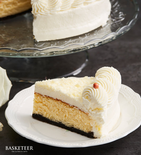 White chocolate cheesecake with dark crust and creamy layers, topped with white chocolate shavings and piped frosting for