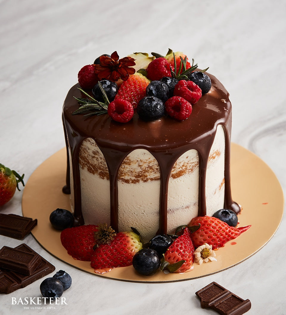 Mini dark chocolate drip cake with fresh berries, raspberries, and rosemary on light cake board