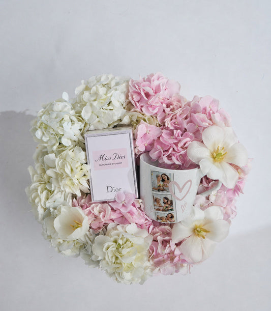 Luxury flower arrangement with Miss Dior perfume box, pink and white hydrangeas, peonies, and photo cards on white background.