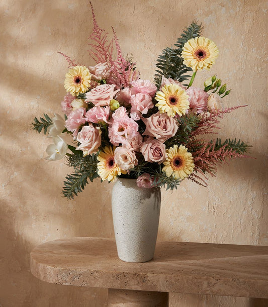 Pastel pink and yellow flowers in grey ceramic vase with roses, gerberas, and feathery astilbe