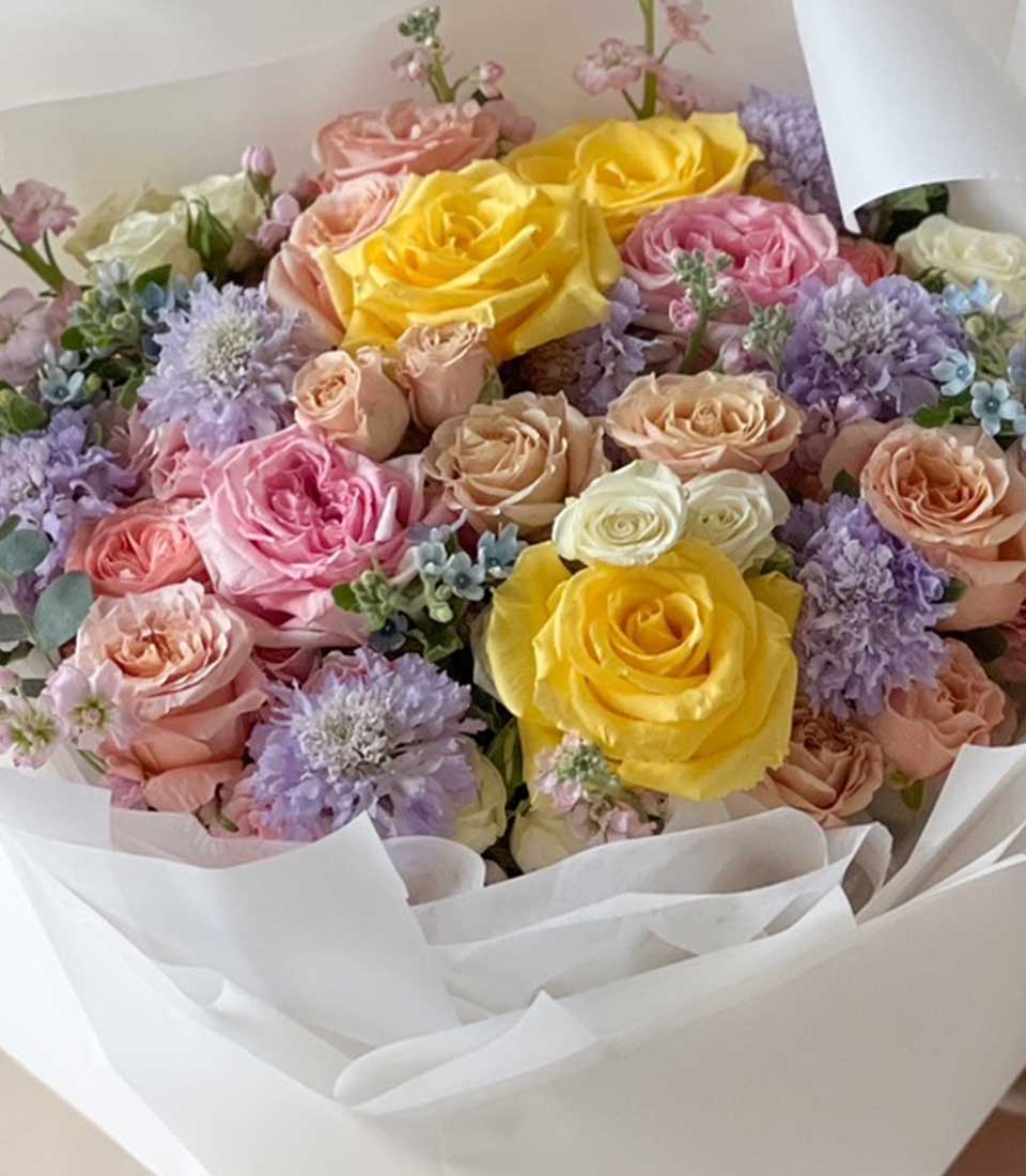 Pastel rose bouquet with yellow, pink, peach and white blooms, wrapped in white tissue paper