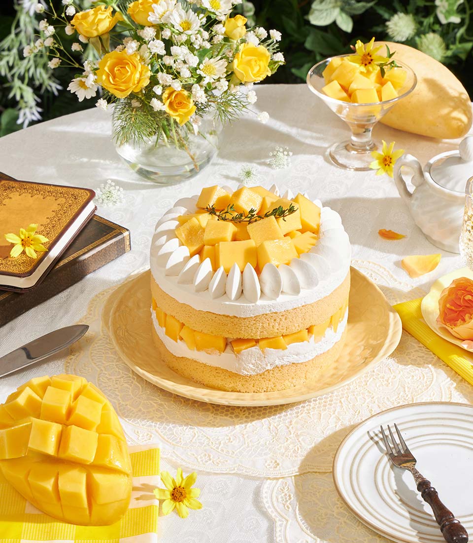 Golden mango layer cake with cream frosting and fresh mango, yellow roses, and afternoon tea styling