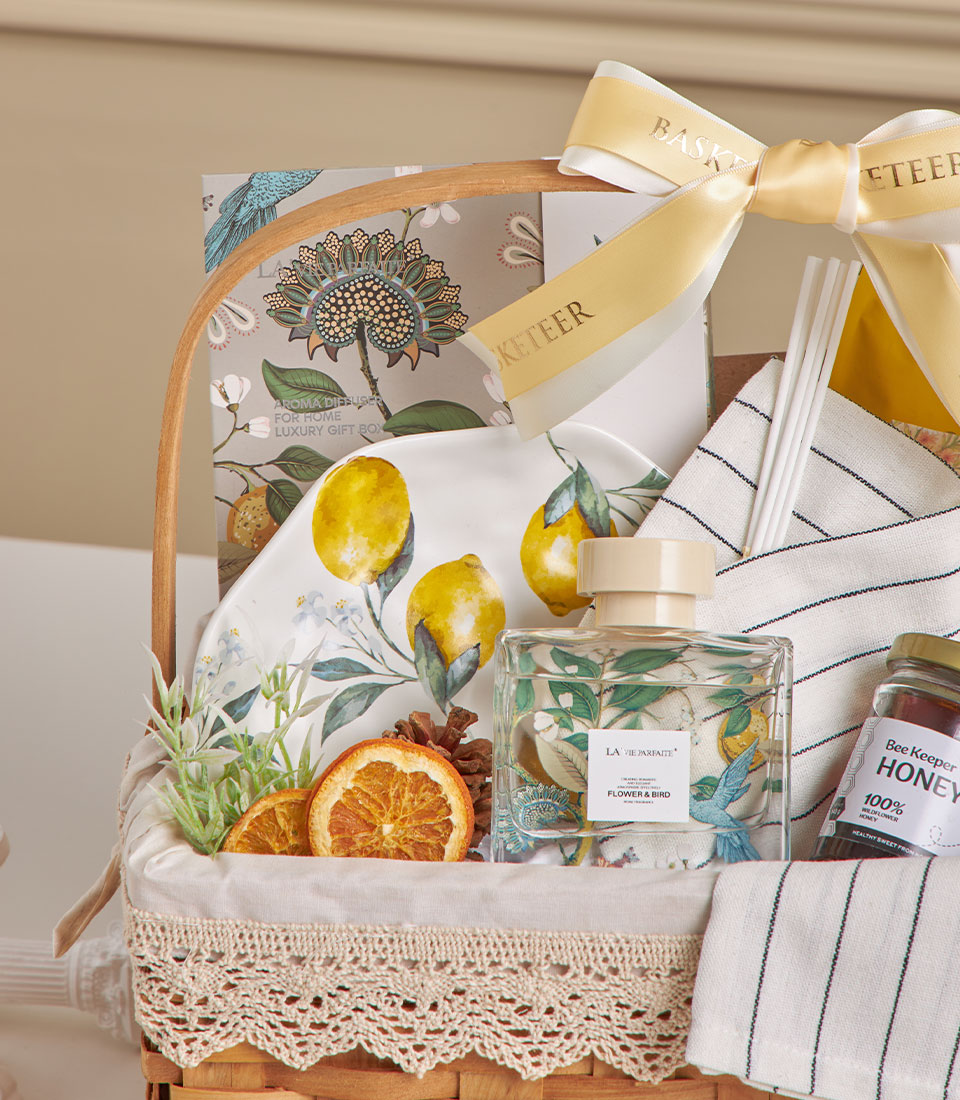 Light brown woven spa gift basket with honey jar, ceramic lemon plate, aroma diffuser, and dried citrus accents tied with