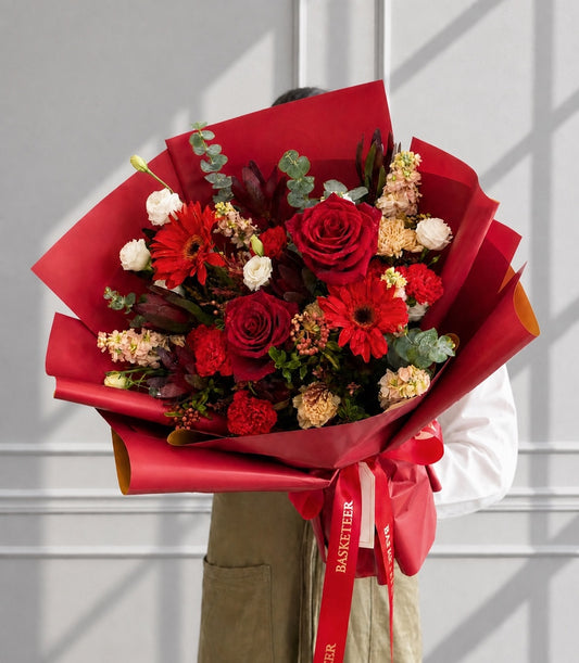 A luxurious red rose bouquet with vibrant gerbera daisies, accented by white and peach