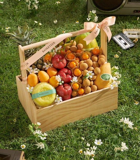 Wooden basket filled with fresh Thai tropical fruits including rose apples, mangoes, longans, and pineapple with pink