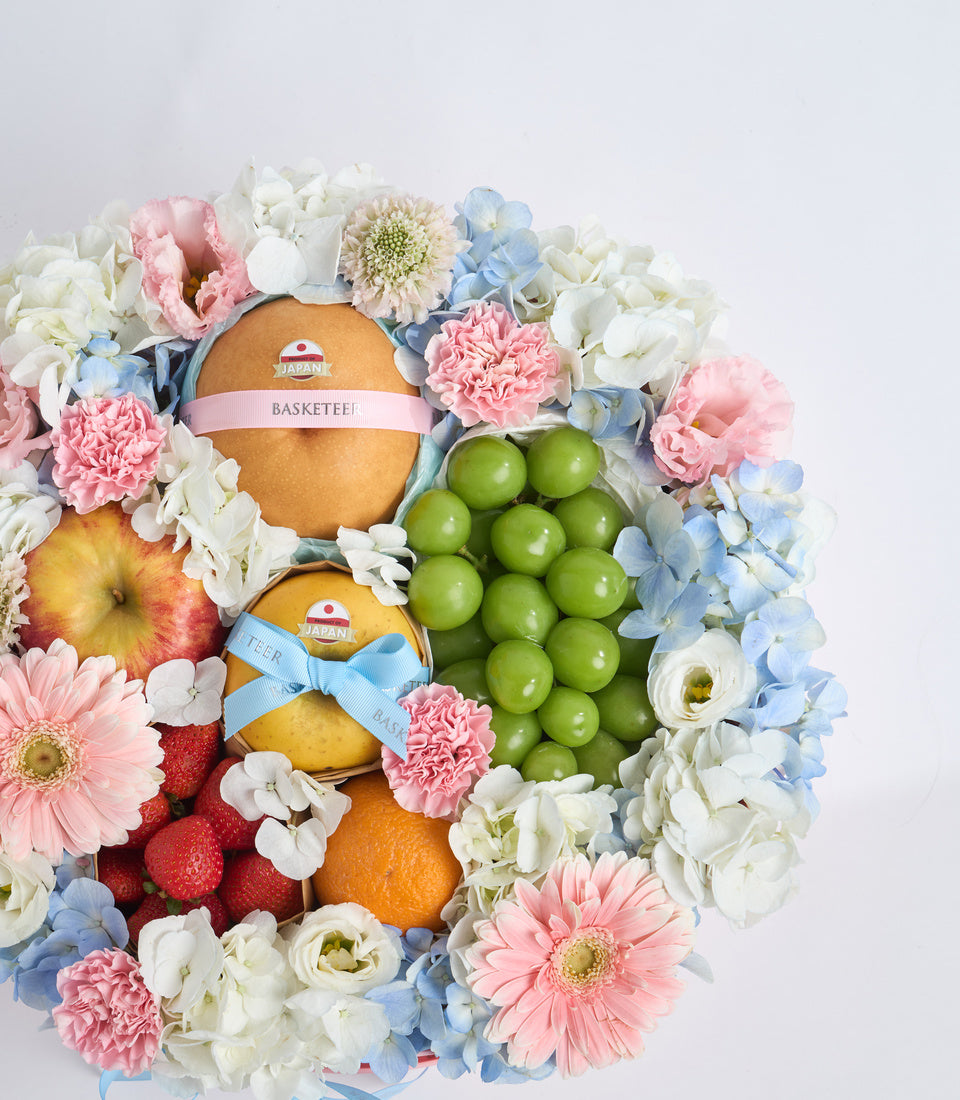 # Alt Text
Luxury fruit and flower gift basket with pink ribbons, featuring fresh apples, oranges, strawberries, green grapes, surrounded by pink carnations, white roses, blue hydrangeas.